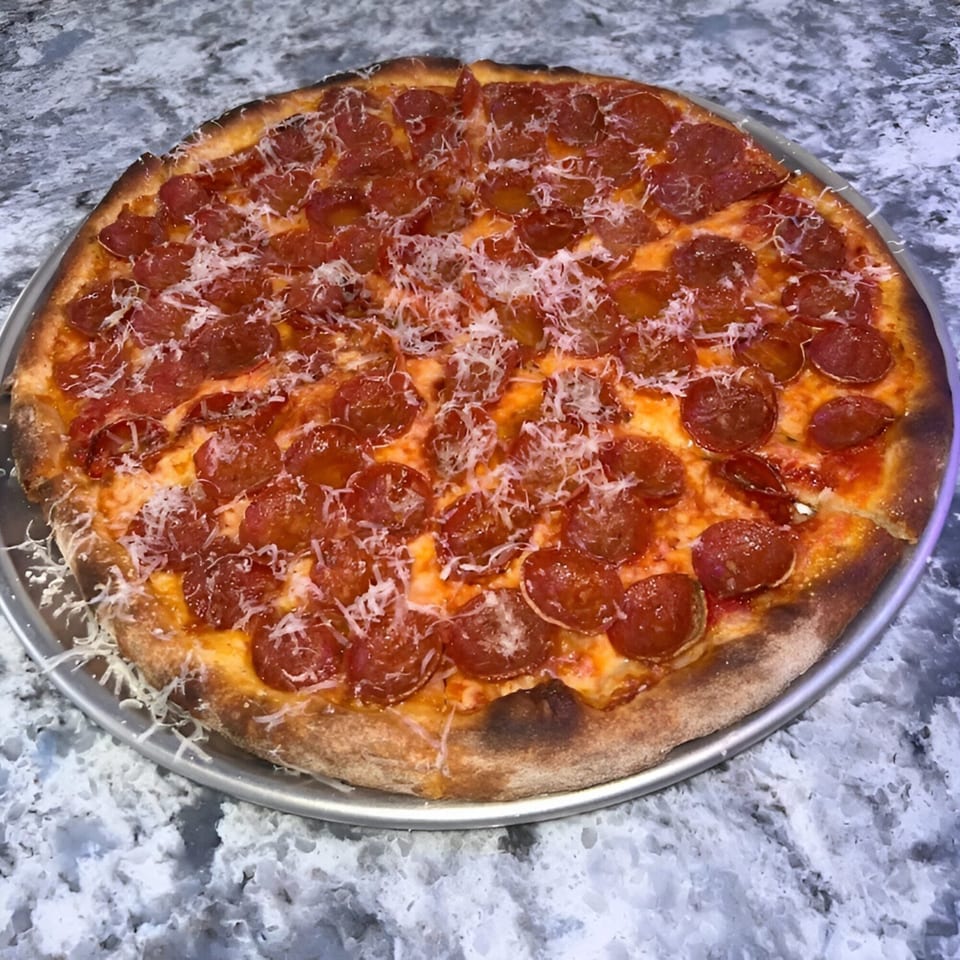 PZZA Boca Raton's pepperoni pizza, topped with shredded parmesan, on a metal pan.