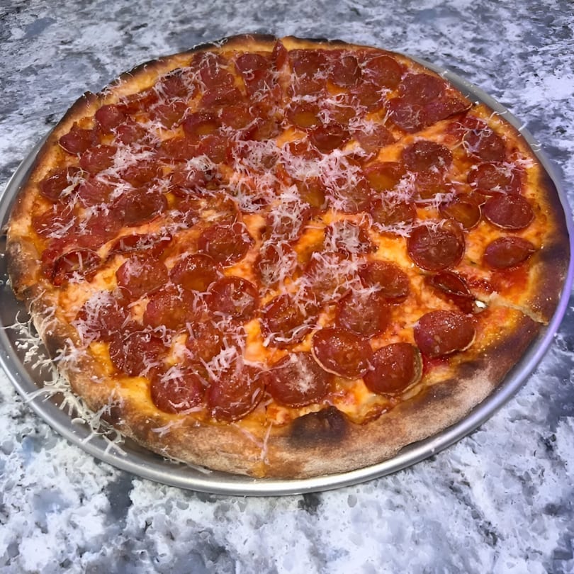 PZZA Boca Raton's pepperoni pizza, topped with shredded parmesan, on a metal pan.
