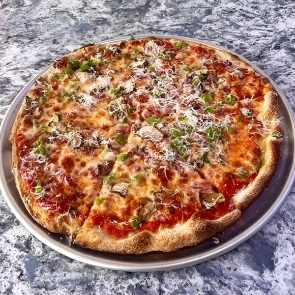 A whole PZZA pizza with green peppers, mushrooms, and shredded cheese on a metal pan.