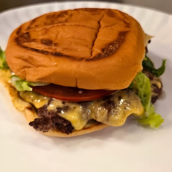 Close-up of a cheeseburger with melted cheese, lettuce, and tomato on a white plate.